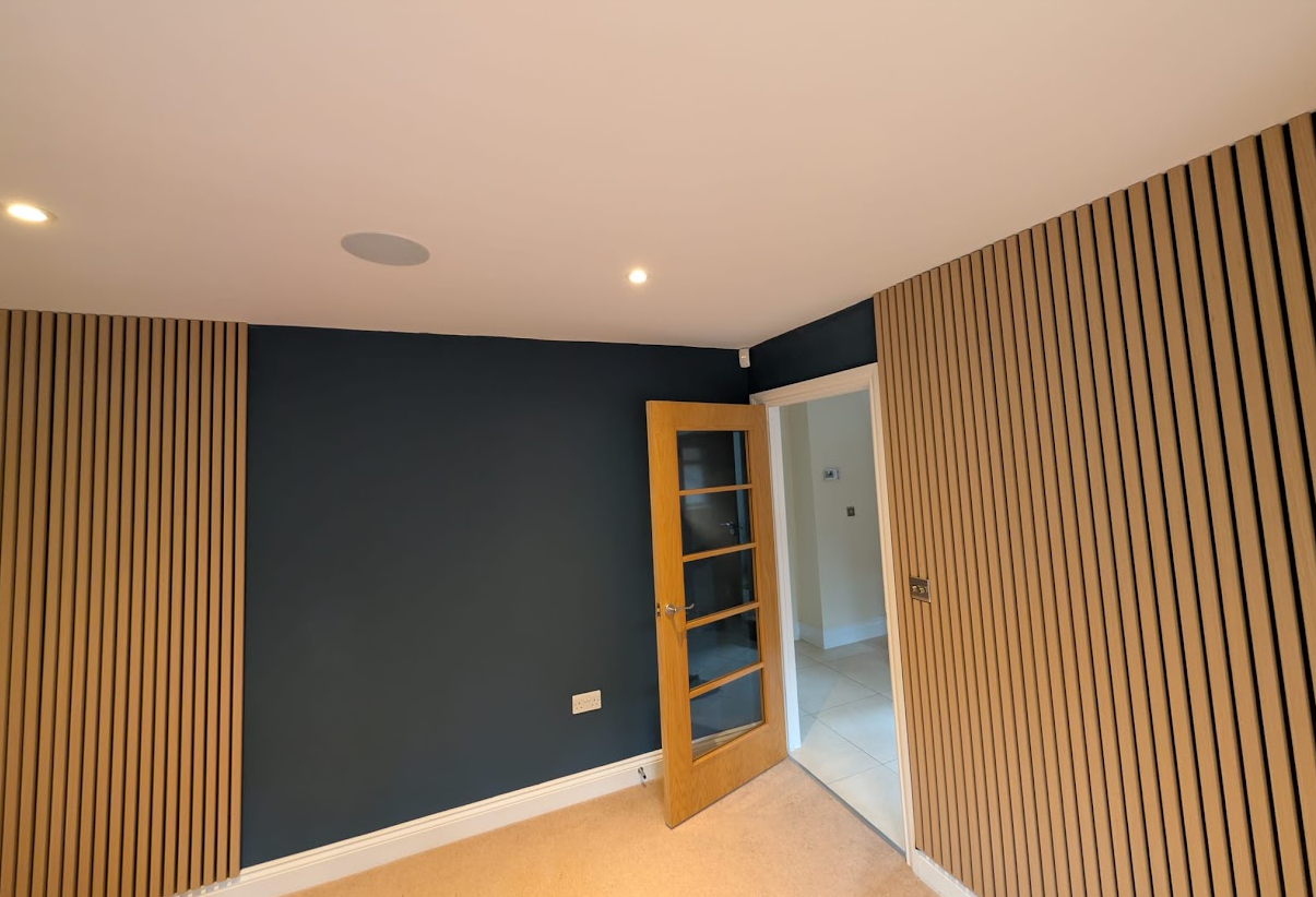 A finished Roomwright interior with oak acoustic wall panelling, a dark feature wall and warm recessed lighting